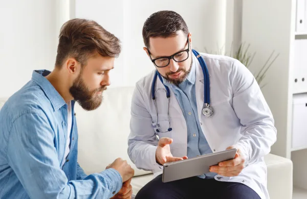 Doctor showing information on a tablet to a male patient during a consultation.
